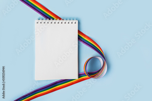 LGBT raibow flag ribbon with notebook or note mock up on light blue background. Flat lay, top view, trendy minimal composition, concept of gay pride of proud month lgbtq community. Cultural divesity photo