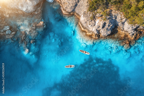 Fototapeta Naklejka Na Ścianę i Meble -  Aerial view of people on floating kayaks on blue sea, rocky coast, trees at sunset in summer. Blue lagoon, Oludeniz, Turkey. Tropical landscape. Sup boards on clear water. Top view of canoe. Tourism