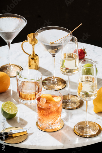 Negroni, martini cocktail (garnished with olive), Martinez (garnished with lavender) and Prosecco, on a carrara white marble table