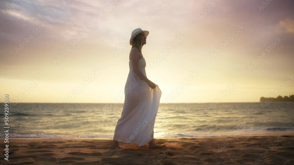 Young beautiful American woman in love getting married on ocean beach at cinematic golden sunset above horizon. Marriage, love, romance, summer vacation by sea RED 6K video. Lady in white boho dress 