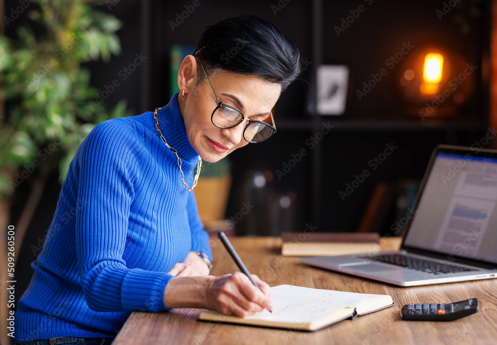 Middle aged businesswoman working at laptop, take notes in home office Middle aged businesswoman working at laptop, take notes in home office