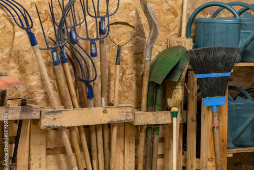 Forks, shovels, broom, watering can, gardening tools, stored in a shelter