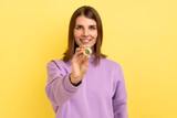 Look at that. Surprised excited woman standing holding bitcoin, paying attention at new digital cryptocurrency, wearing purple hoodie. Indoor studio shot isolated on yellow background.