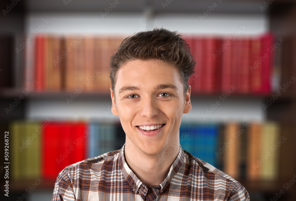 Happy schoolboy guy posing in campus library on bookshelves background. Happy schoolboy guy posing in campus library on bookshelves background.