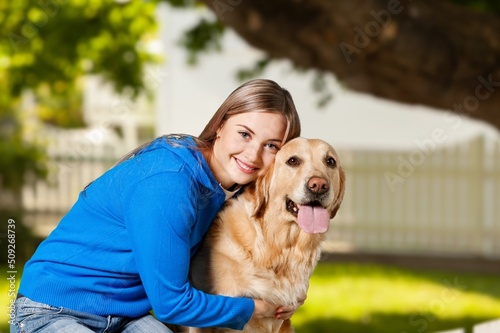 Teen girl hugging dog at the nature and smiling. Pretty young female with doggy pet in the sunny field