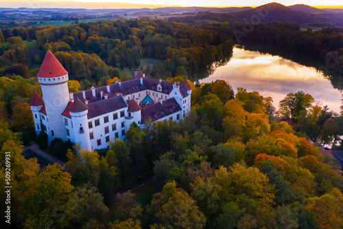 Autumn forest landscape overlooking ancient Konopiste castle on shore of lake in morning, Benesov, Czech Republic. View from drone..