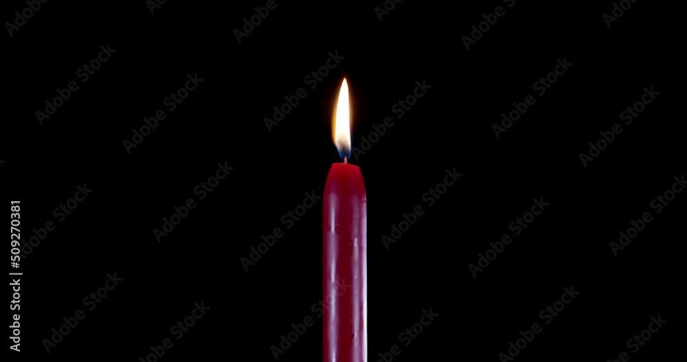 A single red candle burning. Isolated candle burning with dark background. Red paraffin candle with yellow shades burns on a black background. Background or illustration of remembrance or celebration. A single red candle burning. Isolated candle burning with dark background. Red paraffin candle with yellow shades burns on a black background. Background or illustration of remembrance or celebration.