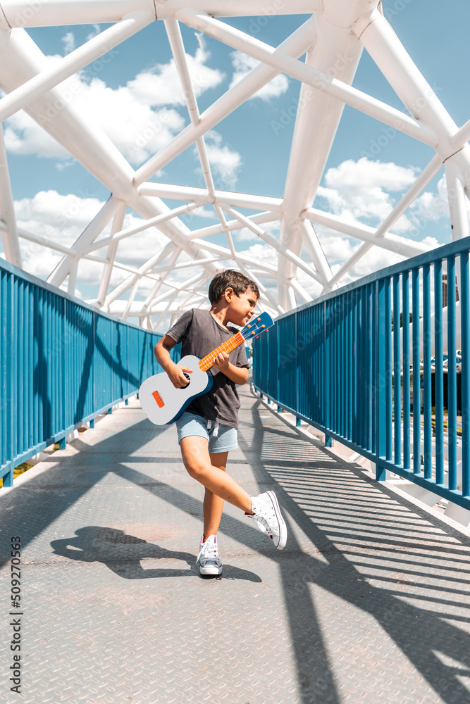 Latino boy posing with a ukulele cross-legged on a bridge in Managua Nicaragua Latino boy posing with a ukulele cross-legged on a bridge in Managua Nicaragua