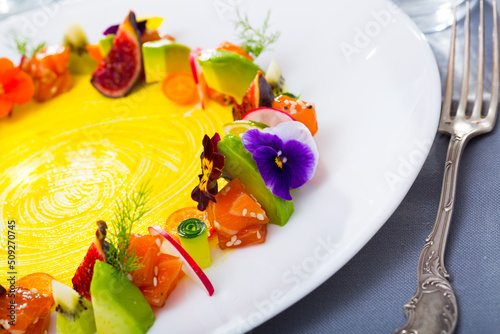 Raw salmon tartare served on white plate with fruits and vegetables garnished with heartsease flowers