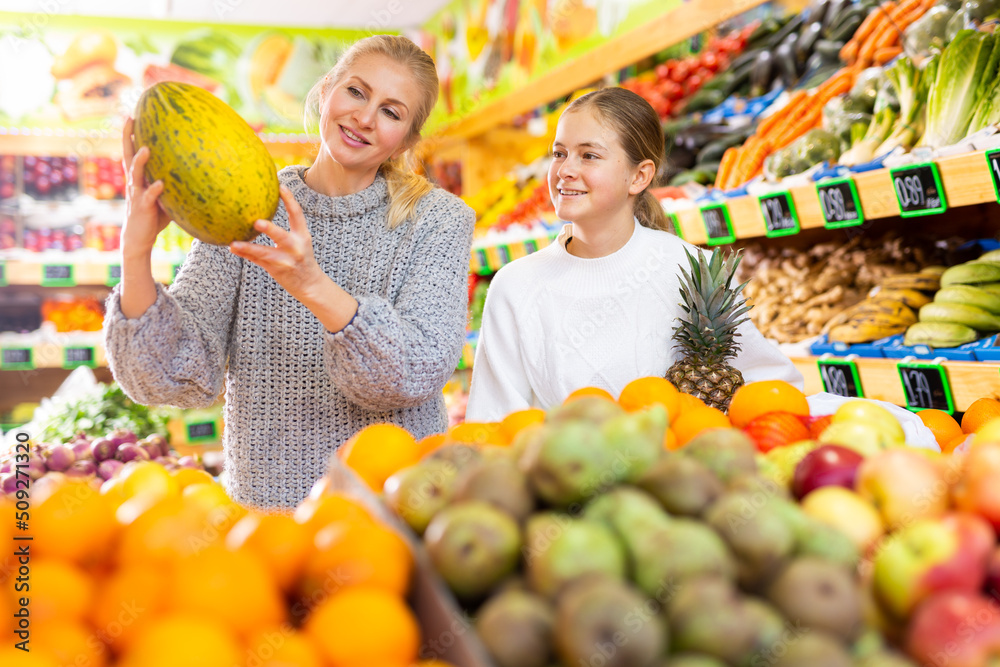 Daughter and mom buy fruit - pineapple and melon at the grocery store