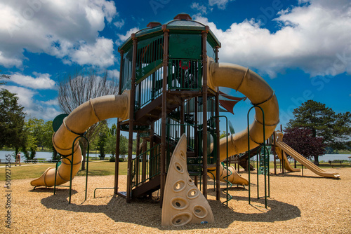 a brown and green jungle gym on the playground at the park surrounded by lush green trees, grass and plants with blue sky and clouds at Cauble Park in Acworth Georgia USA photo