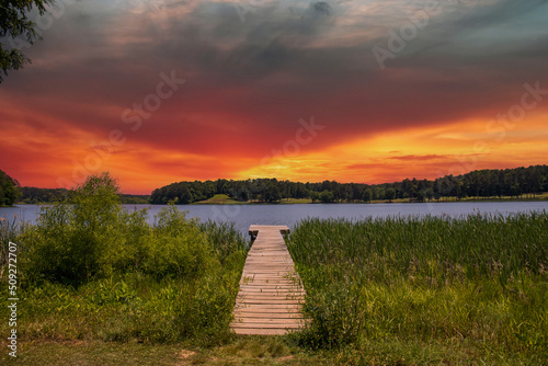 a brown wooden dock over the rippling blue waters of Lake Acworth surrounded by lush green trees and blue with powerful clouds at sunset at Cauble Park in Acworth Georgia USA photo