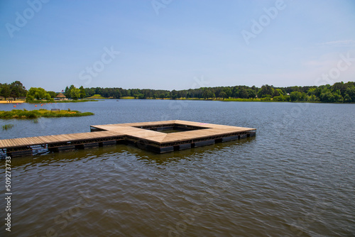 a long square brown wooden dock over the rippling waters of Lake Acworth surrounded by lush green trees and grass with a gorgeous clear blue sky at Cauble Park in Acworth Georgia USA photo