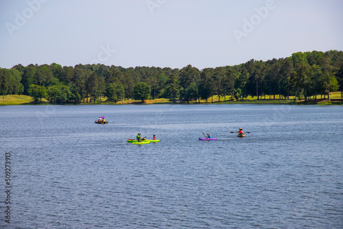 people on color kayaks rowing on the vast blue lake water surrounded by lush green trees and grass with blue sky at Cauble Park in in Acworth Georgia USA photo