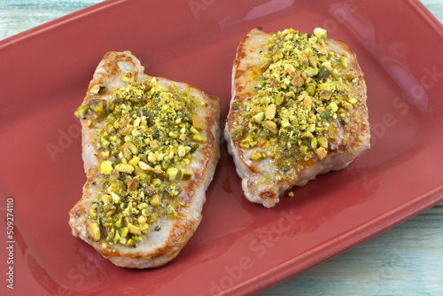 Two boneless pork chops with crushed pistachios on red serving plate