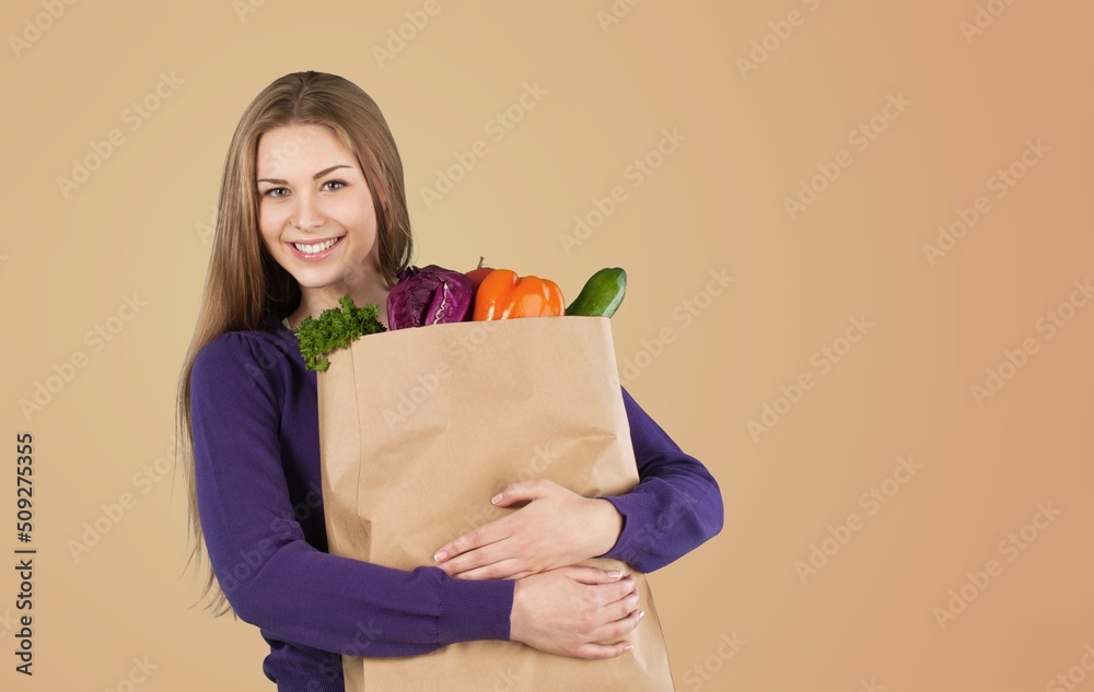 Young smiling vegetarian woman hold paper bag with vegetables after shopping Young smiling vegetarian woman hold paper bag with vegetables after shopping