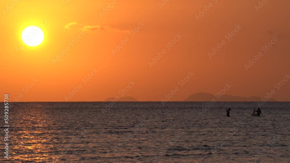 Local Fishermen In The Ocean Under Giant Bright Orange Sun At Sunset. - wide Local Fishermen In The Ocean Under Giant Bright Orange Sun At Sunset. - wide