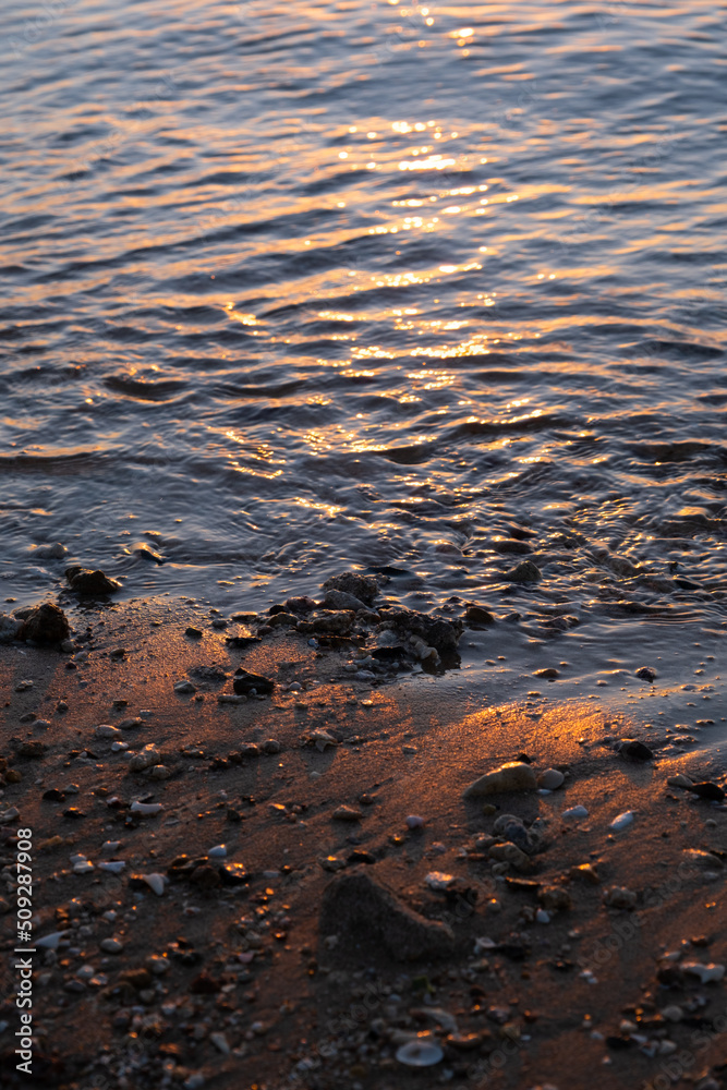 Red Sea close up view. Sea wave nailed stones to the sandy beach. Vertical photo. Reflection of the sunset in the waves.
