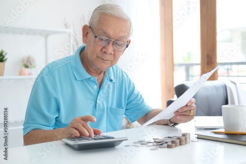 Serious man sitting at table near utility bill and calculating expenses