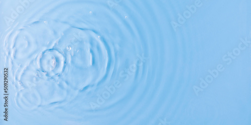 Drops fall down into clear fresh water on light blue background view from above