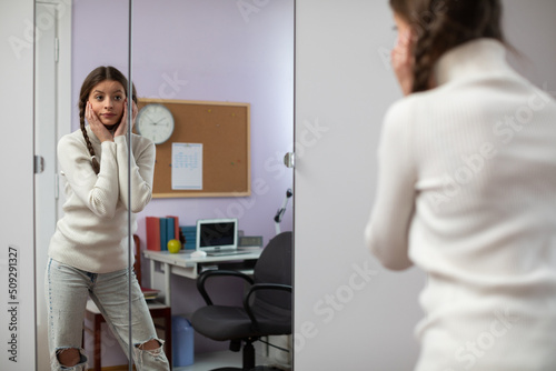 Fashion girl tunes up in front of the mirror and makes different faces.