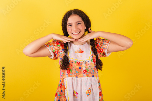 Girl wearing traditional orange clothes for festa junina. in a sweet and cute pose with her hands on her chin. photo