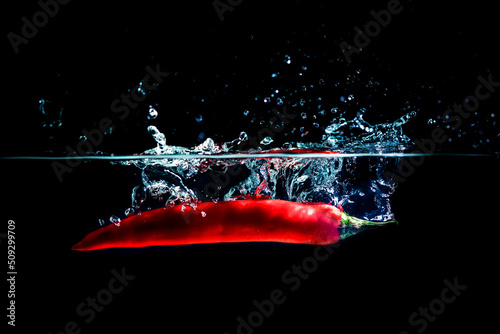 Close up of hot chili pepper fell into the water and the water splashed up with black background.
