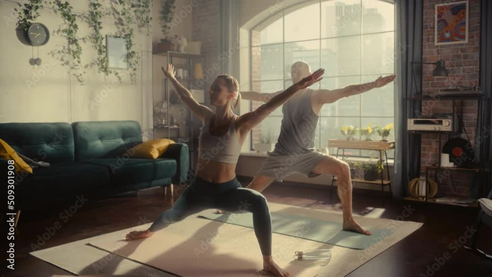 Young Athletic Couple Exercising, Stretching and Practising Yoga in the Morning in Bright Sunny Home Living Room. Healthy Lifestyle, Fitness, Wellbeing and Mindfulness Concept. Young Athletic Couple Exercising, Stretching and Practising Yoga in the Morning in Bright Sunny Home Living Room. Healthy Lifestyle, Fitness, Wellbeing and Mindfulness Concept.