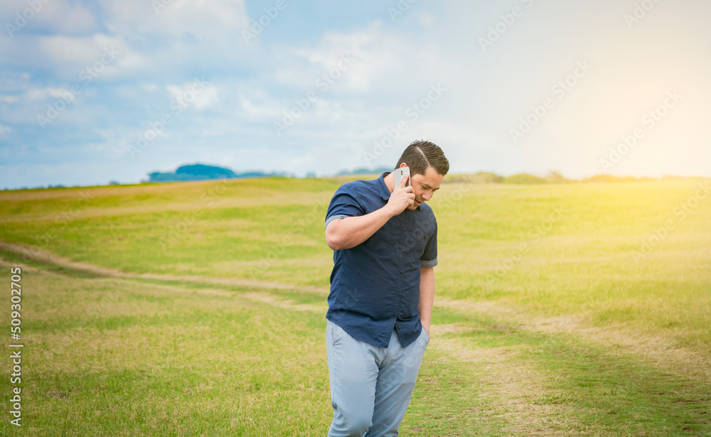 Person with his cell phone in the field talking on the phone, Man calling on the phone in the field, man on a road talking on the phone, young person talking on the phone in a field