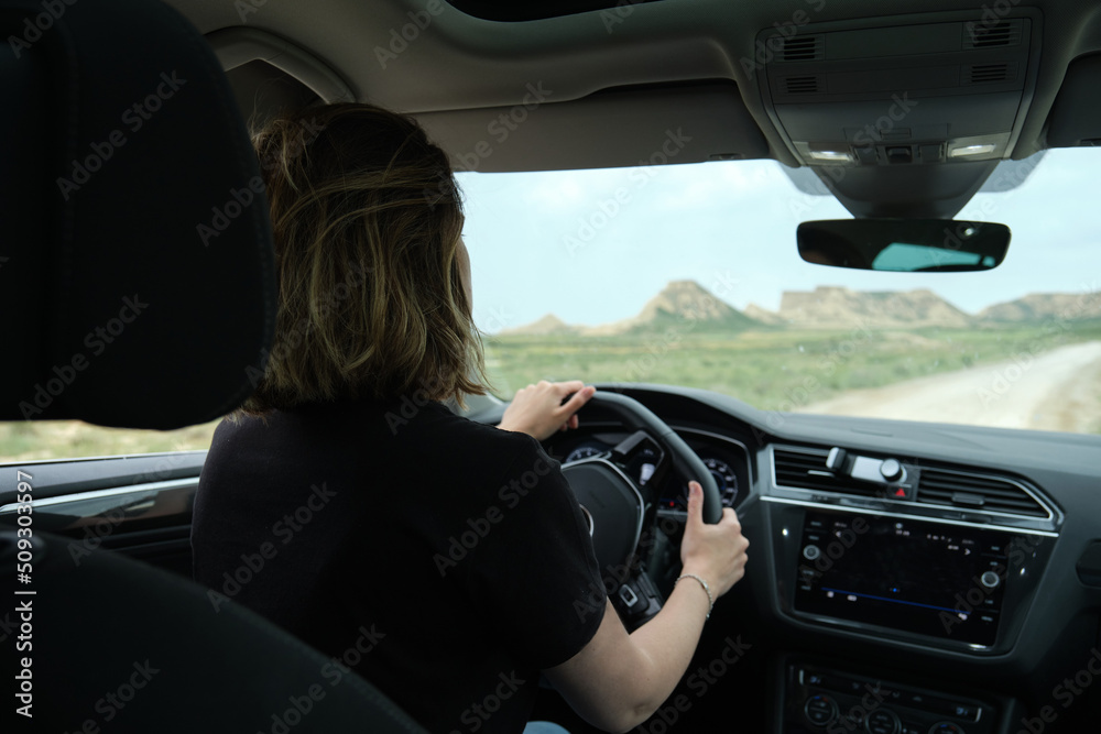 Woman driving a car while traveling on the desert road with a rocky landscape in the background. road trip vacation