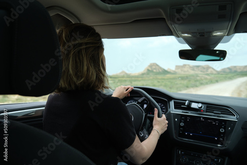 Woman driving a car while traveling on the desert road with a rocky landscape in the background. road trip vacation