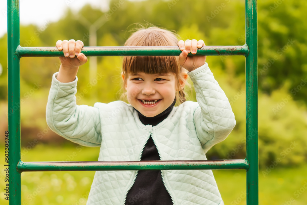 Charming 4-year-old Caucasian little girl having fun on the playground and smiling. A cheerful little girl is standing on the step of the stairs on the playground. Happy childhood.Active outdoor games Charming 4-year-old Caucasian little girl having fun on the playground and smiling. A cheerful little girl is standing on the step of the stairs on the playground. Happy childhood.Active outdoor games
