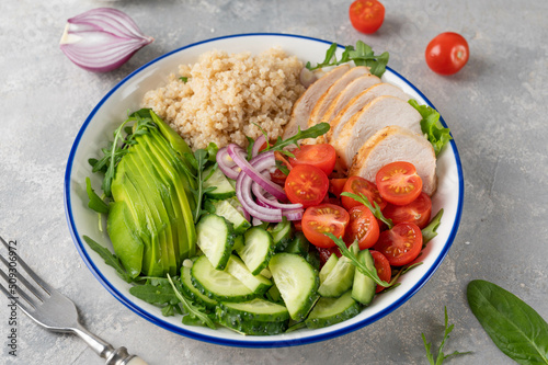 Healthy bowl lunch with grilled chicken, quinoa, avocado, tomatoes, cucumbers and fresh arugula on gray background. Top view. Selective focus.