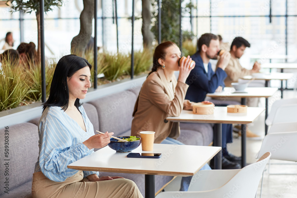 Group of people sitting in row at food court in shopping mall cafe area, copy space