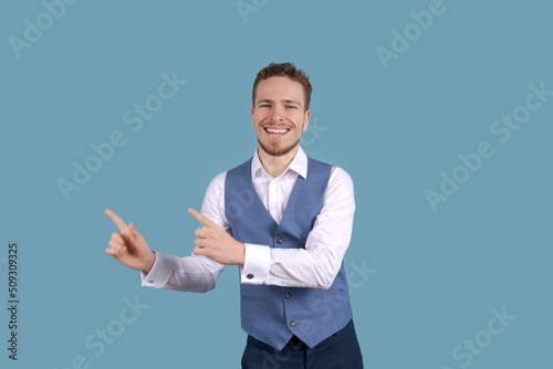 Wow this is incredible. Shocked caucasian business man smiling pointing aside gesture in copy space wearing white shirt and blue jet on blue background