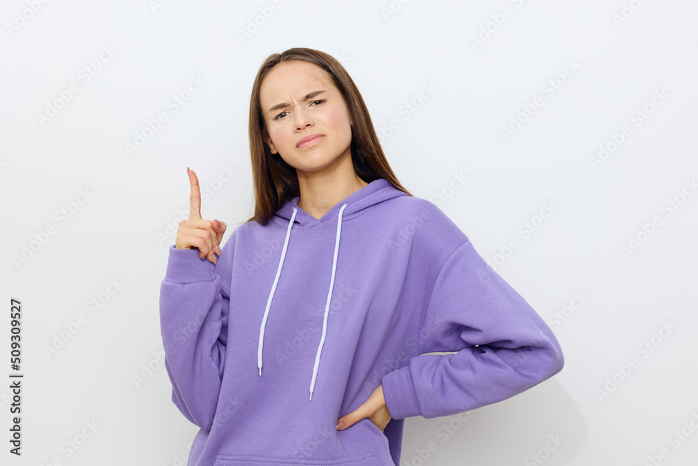 frowning a little, the woman stands on a white background in a purple tracksuit and points up with her index finger, putting her other hand on her hip, looking forward with displeasure frowning a little, the woman stands on a white background in a purple tracksuit and points up with her index finger, putting her other hand on her hip, looking forward with displeasure