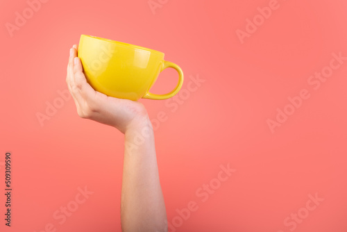 Photo of yellow cup coffee in hand isolated on pink background. Banner design. Cup of tea