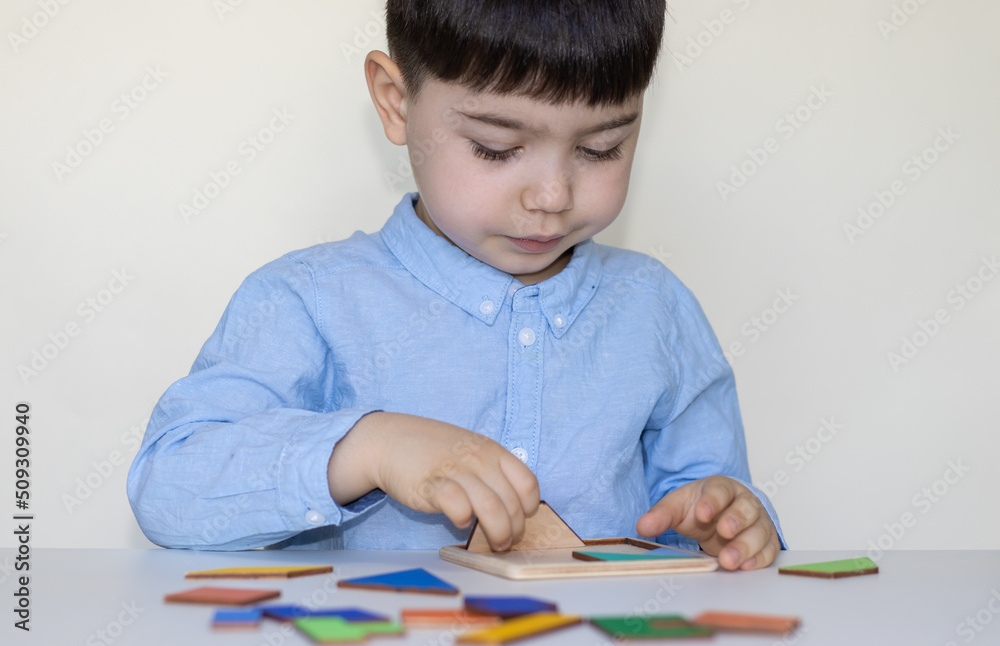 cute serious face little boy at white table playing with tangram puzzle.puzzle of seven flat polygons,tans,form shapes.educational,logic game for kids.back to school,kindergarten cute serious face little boy at white table playing with tangram puzzle.puzzle of seven flat polygons,tans,form shapes.educational,logic game for kids.back to school,kindergarten