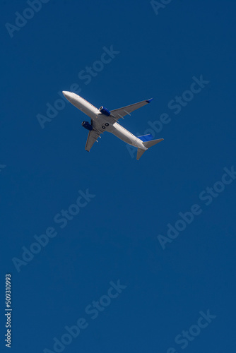Aerial view of white airplane with blue tail, shot from below with selective focus.