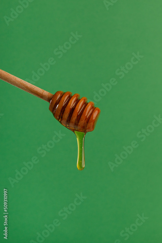 Honey flowing, dripping from wooden dipper stick over green background