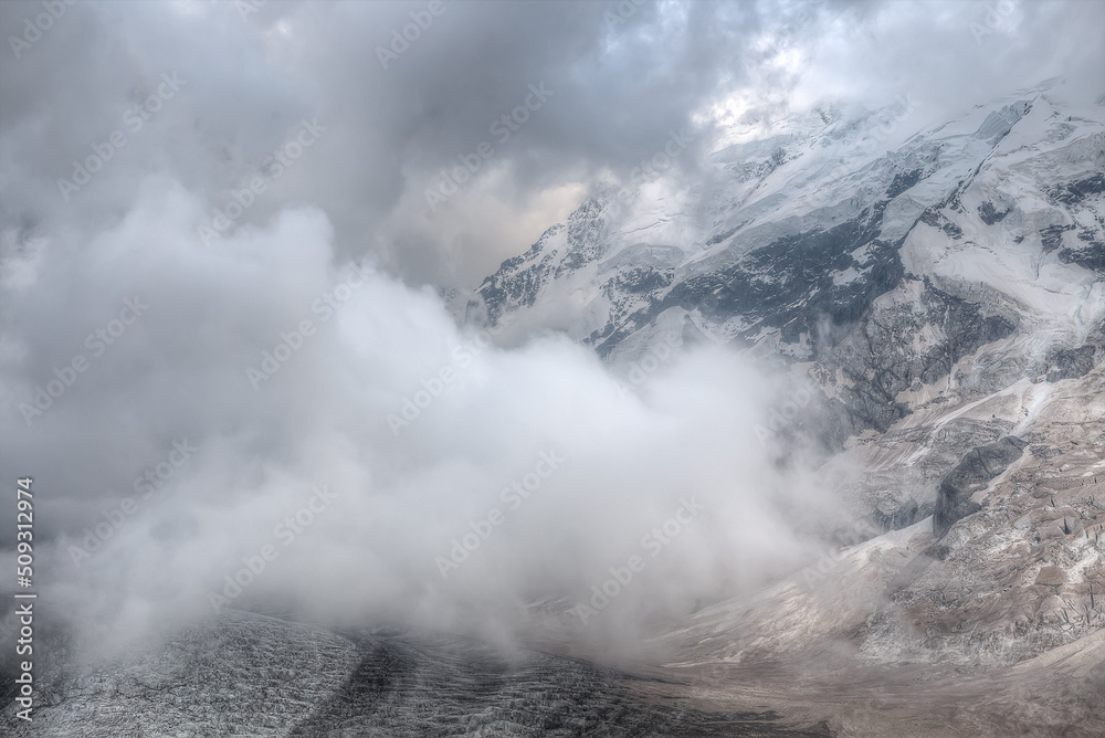 A large cloud hangs over the glacier. In the background is a high mountain with snow-capped peaks. A large area of â€‹â€‹the frame is occupied by a hazy image of a cloud. soft focus.
