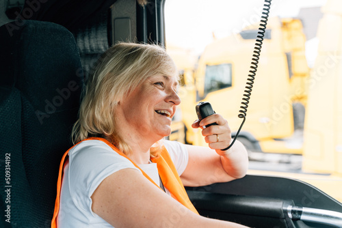 Woman truck driver talking by radio inside the cabin. Female trucker job worker photo