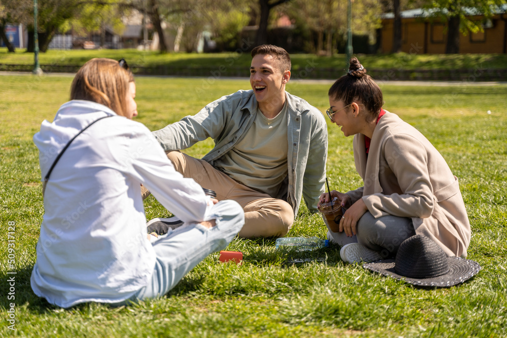 Friends spending time together while drinking coffee in the park.Sitting on green grass Friends spending time together while drinking coffee in the park.Sitting on green grass