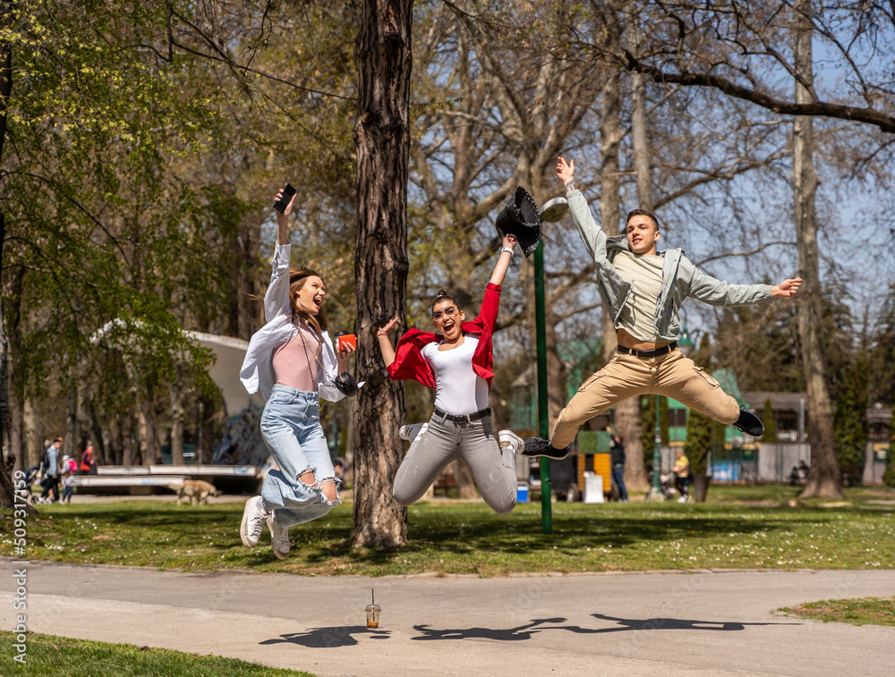 Obraz premium Friendship, freedom, happiness and people concept - group of happy friends dancing and jumping in park