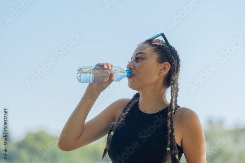 Portrait of a happy female athlete drinking water from a plastic bottle after an outdoor workout
