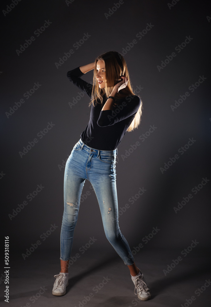 Attractive female model in denim jeans posing isolated on grey background.