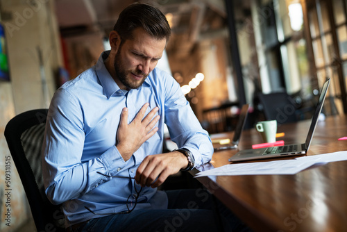 oung businessman having chest pain. Man sitting in the office working on laptop.