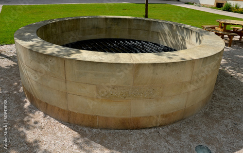 stone round fountain with a protective grid of twisted prisms. forged steel bars go spiraled at the top. around the well there is a retaining wall and a lawn. protection against falling into the depth © Michal
