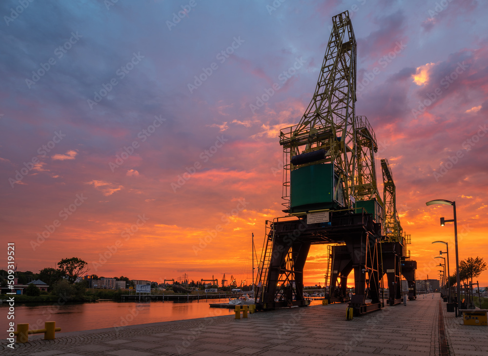Historic harbour cranes on riverside boulevards in Szczecin during a dramatic sunrise