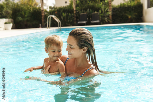Mother and her cute little son swimming in outdoor pool during summer vacation